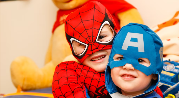 Two children wearing superhero costumes and smiling.